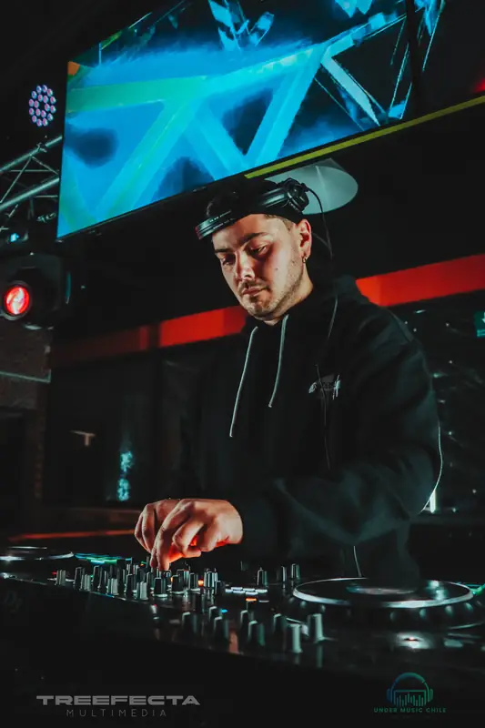 DJ con audífonos frente a una pantalla con visuales, en plena sesión